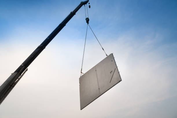 Construction site crane is lifting a precast concrete wall panel to installation building. Construction site crane is lifting a precast concrete wall panel to installation building. prefabricated building stock pictures, royalty-free photos & images