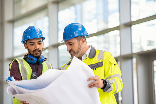 Construction site worker and engineer discussing on blueprint project stock photo