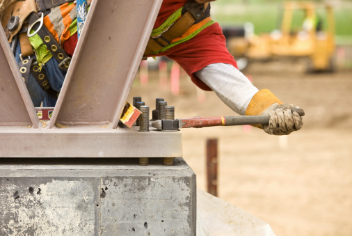 A construction worker is securing a steel support column onto a piling with a pipe wrench and nut. This was shot at a commercial construction site and would work well for a bridge or other steel structure.