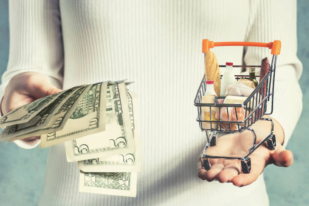 소비자 바구니 가치 개념. 소녀는 그녀의 손에 돈과 쇼핑 바구니를 무게 - inflation 뉴스 사진 이미지