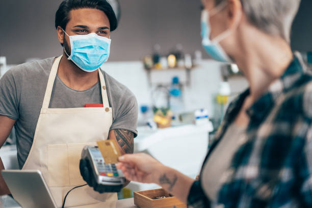 Contactless payment and Coronavirus Young barista and Modern woman paying contactless at cafe wearing face protective mask to prevent Coronavirus and other diseases consumer behavior stock pictures, royalty-free photos & images