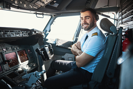 Cheerful Caucasian man sitting in the cockpit with his arms crossed and smiling cheerfully