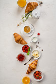Continental breakfast captured from above top view, flat lay . Coffee, orange juice, croissants, jam, berry, milk and flowers. Grey stone worktop as background. Layout with free text copy space.