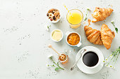 Continental breakfast captured from above (top view, flat lay). Coffee, orange juice, croissants, jam, honey and flowers. Grey stone worktop as background. Layout with free text (copy) space.