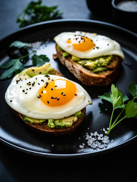 Continental breakfast - sunny side up eggs on toasted bread with avocado on black background stock photo