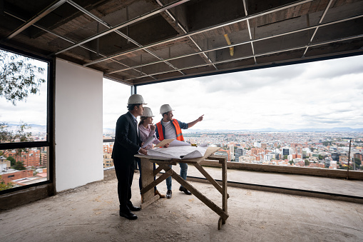 Contractor, architect and engineer working together as a team at a construction site and pointing at the windows while looking at a blueprint - housing development concepts