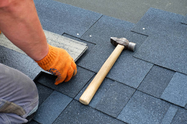 Contractor hands installing bitumen roof shingles using hammer in nails. stock photo