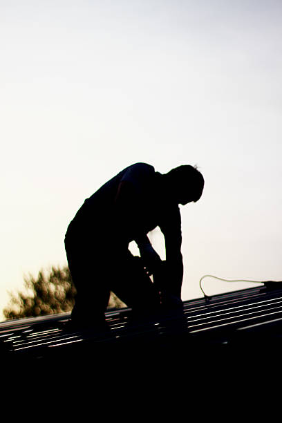 Contractor in Silhouette working on a Roof stock photo