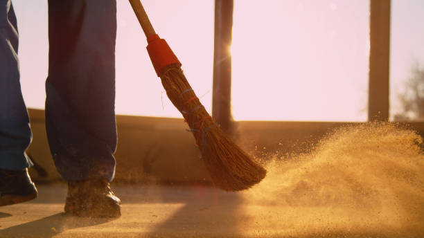 LOW ANGLE: Contractor sweeping the dirty floor with a straw broom at sunset. stock photo