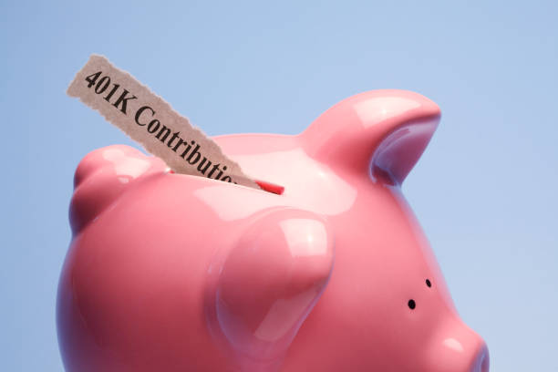 401K Contribution "401K Contribution" printed on a torn piece of paper that is inserted into the coin slot of a pink piggy bank against a blue background. 401k stock pictures, royalty-free photos & images