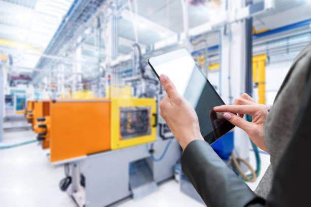 Control & touchpad in factory Horizontal color image of businesswoman - unrecognizable person - working with digital tablet in large futuristic factory. Focus on businesswoman's hands holding black tablet, futuristic machines in background. power supply stock pictures, royalty-free photos & images