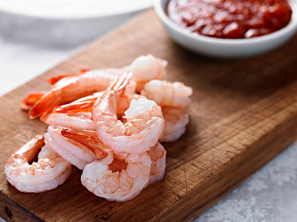 Cooked shrimps on wooden board next to red sauce Close up of Shrimp Cocktail with Sauce in the Background. shrimp cocktail stock pictures, royalty-free photos & images