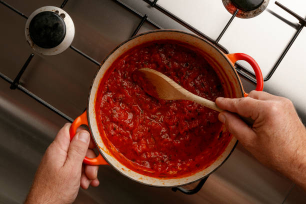 Cooking a traditional gormet tomato sauce and wooden spoon, on a stainless steal hob Cooking a traditional gormet tomato sauce and wooden spoon, on a stainless steal hob, shot from above sauce stock pictures, royalty-free photos & images