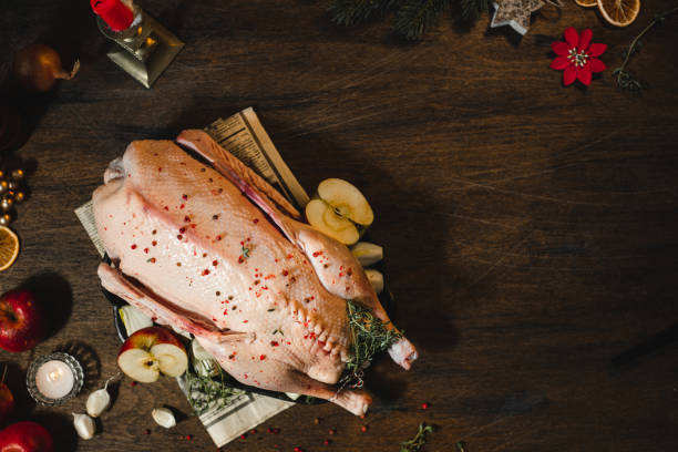 Cooking Christmas dinner Directly above shot of a raw Christmas duck ready to cook with thyme and apples on a wooden table. Cooking christmas dinner in kitchen. duck meat stock pictures, royalty-free photos & images