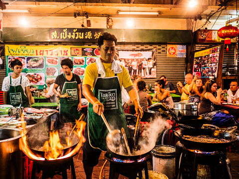 Bangkok, Thailand - February 26, 2016: A cook is preparing food in a restaurants with chairs and tables on the street at Chinatown Bangkok. This area is very popular because the diverse food stands that appear at night time.