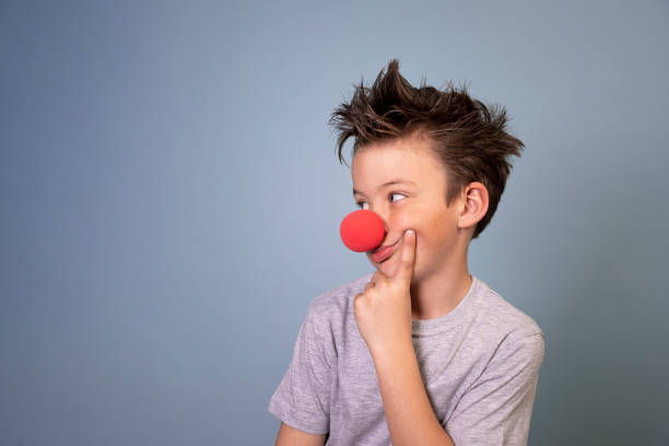 cool boy with wild hair posing with red clown nose on blue background cool boy with wild hair posing with red clown nose on blue background and is happy clown's nose stock pictures, royalty-free photos & images
