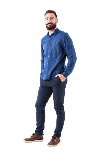 Cool smiling guy, with hands in pockets looking up wearing blue denim shirt and pants. Full body isolated on white background.