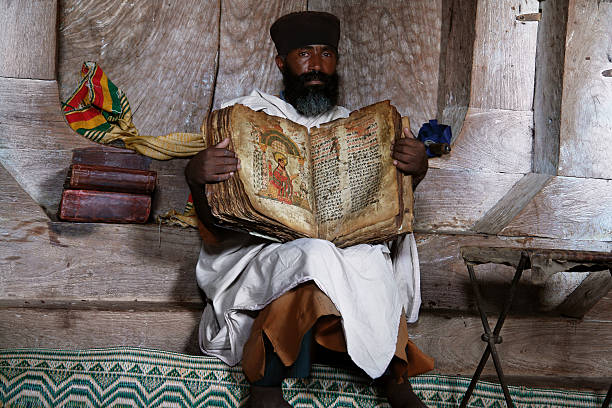 Coptic Priest with Old Bible Lake Tana, Ethiopia - March 22, 2009: Ethiopian Christian Priest Showing Old Bible in the Coptic Orthodox Monastery at the Tana Lake Island coptic stock pictures, royalty-free photos & images