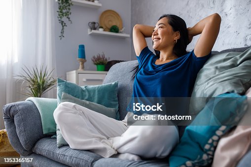istock Copy space shot of young woman lounging on sofa with hands behind head and daydreaming 1353365157