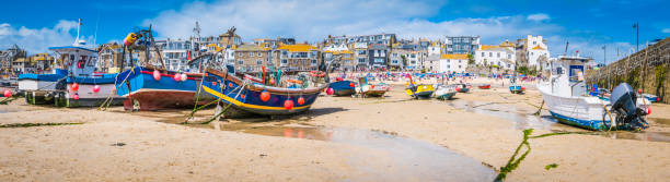 Cornwall St Ives fishing boats and tourists beach harbour panorama Fishing boats moored on the beach in St. Ives harbour, the picturesque seaside resort and fishing village in Cornwall, UK. fishing village stock pictures, royalty-free photos & images