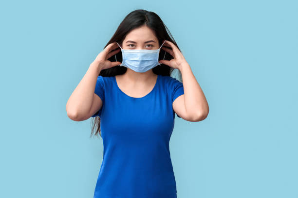 conceito de coronavirus. mulher chinesa colocando máscara médica de pé isolado em cinza sorrindo positivo - máscara covid - fotografias e filmes do acervo