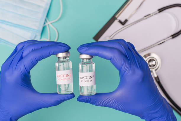 coronavirus aşısı test kavramı inceleyerek. üst üstte maskeleri stetoskop ve mavi teal arka plan üzerinde izole pano ile şişeleri tutan doktor görünümü fotoğraf - covid variant stok fotoğraflar ve resimler