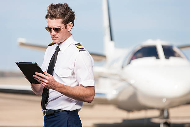 Corporate Pilot Using Electronic Tablet A male pilot stands outside of a corporate jet aircraft, using a modern digital tablet to update his flight plan and preflight checklist. pilot stock pictures, royalty-free photos & images