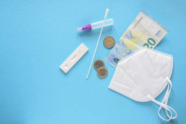 Costs for health care and safety during coronavirus pandemic, covid-19 rapid test, medical ffp2 face mask, and some euro money on a blue background, copy space, high angle view from above stock photo