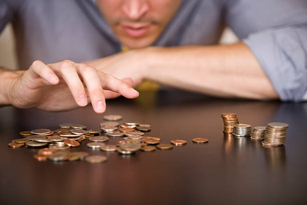 Counting or sorting coins, with 4 piles of different types A man counts his coins on a tabletop. counting stock pictures, royalty-free photos & images