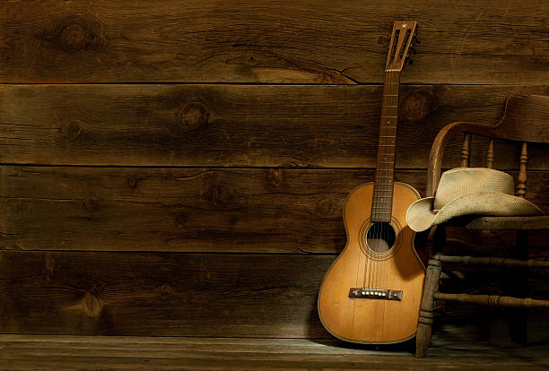 Country and Western Music scene w/chair,hat,guitar-barnwood background (this is a four image stitch) This is a Country and Western theme panorama spot lighting the vintage guitar and cowboy hat. The dark barn wood offers space for over printing. country and western music stock pictures, royalty-free photos & images