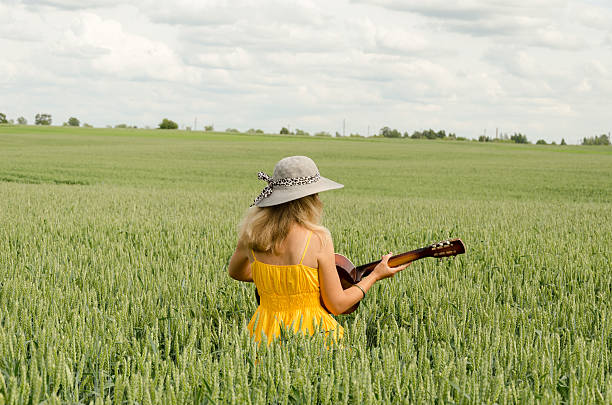 Country girl in dress play guitar wheat field stock photo
