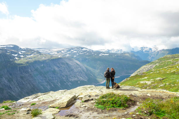 Couple and young dog standing on top of hill surrounded by nature in Norway stock photo