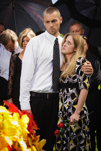 A grieving couple standing graveside at a funeral.