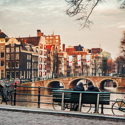Amsterdam - December 7, 2015: Couple back portrait sitting on a bench at sunset in Amsterdam