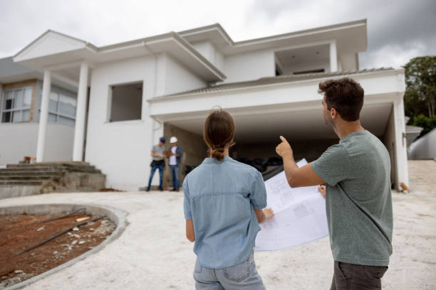 Couple building their dream house and pointing at details while holding blueprint stock photo