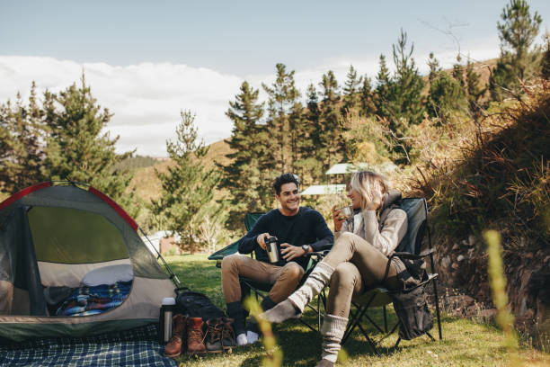 Couple camping in forest Man and woman sitting in chairs outside the tent having coffee and talking. Couple camping in forest. eco tourism stock pictures, royalty-free photos & images