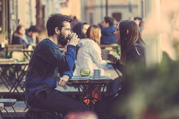 A couple drinking coffee at a picnic table in Stockholm Hipster couple drinking coffee in Stockholm old town. They're sitting face to face. The man is wearing a blue sweater and the woman a striped shirt with black leather jacket. beautiful swedish women stock pictures, royalty-free photos & images