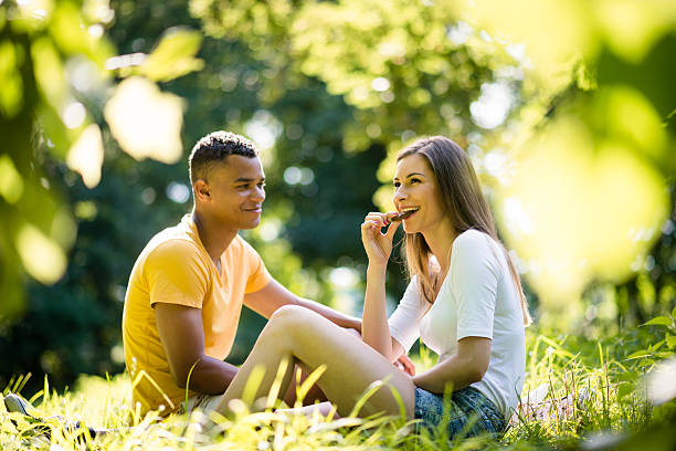 Couple eating chocolate Young couple eating chocolate and sitting in grass on date in park couple eating chocolate stock pictures, royalty-free photos & images