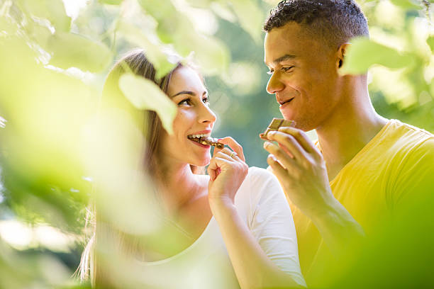 Couple eating chocolate together Young couple eating chocolate on date outdoor in nature couple eating chocolate stock pictures, royalty-free photos & images