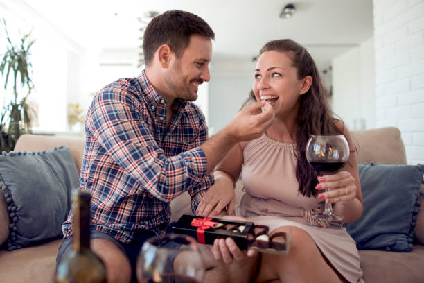 Couple enjoying at home Young happy couple together sitting on sofa-man gives chocolate to woman. couple eating chocolate stock pictures, royalty-free photos & images