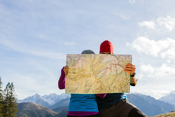 Couple hikers with map in mountains Man and woman hikers hiking in mountains. Young couple looking at map and planning trip or get lost. Selective focus on a map. person looking at map stock pictures, royalty-free photos & images