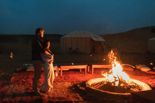 Couple hug in love near big campfire. Romantic night in glamping desert camp in Sahara, Morocco. Honeymoon. stock photo