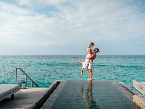 Couple enjoying tropical vacations from the edge of an infinity pool in private over water villa. People travel luxury holidays