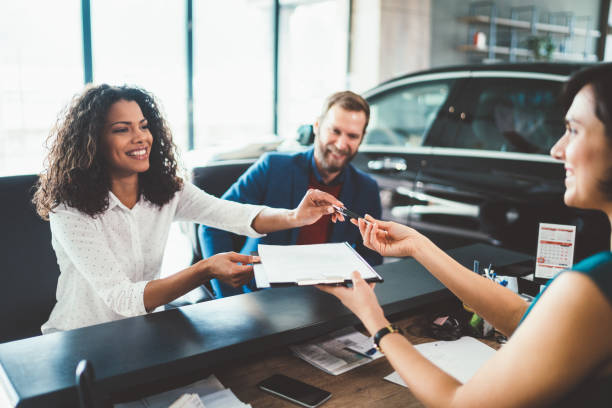 Couple in the showroom buying new car Young woman with her husband signing contract for buying a car car rental stock pictures, royalty-free photos & images