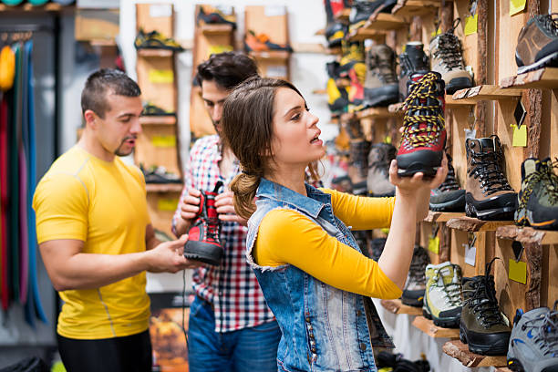 Couple in the store choosing hiking boots Young couple in sports and outdoor store choosing hiking boots and store clerk is helping out with model description. chain store stock pictures, royalty-free photos & images