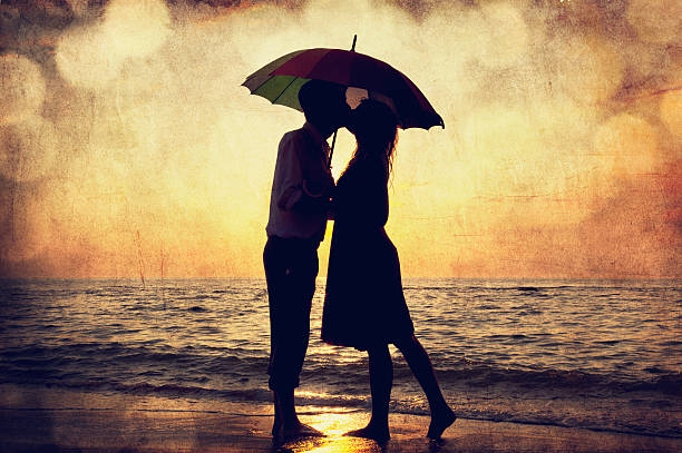 Couple kissing under umbrella at the beach in sunset. stock photo