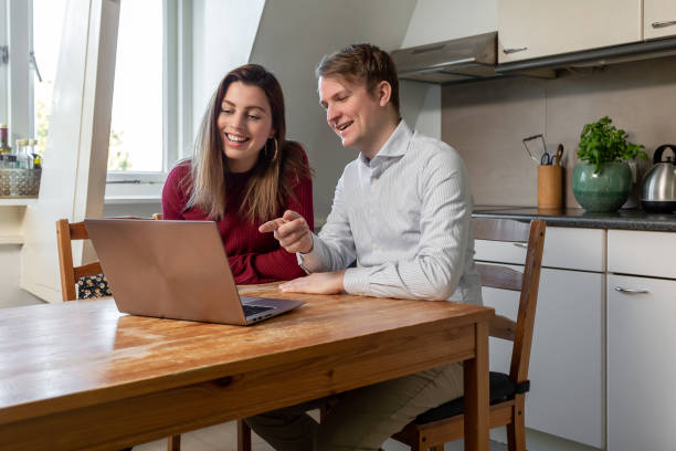 Couple laughing and looking at a laptop at the dining table stock photo