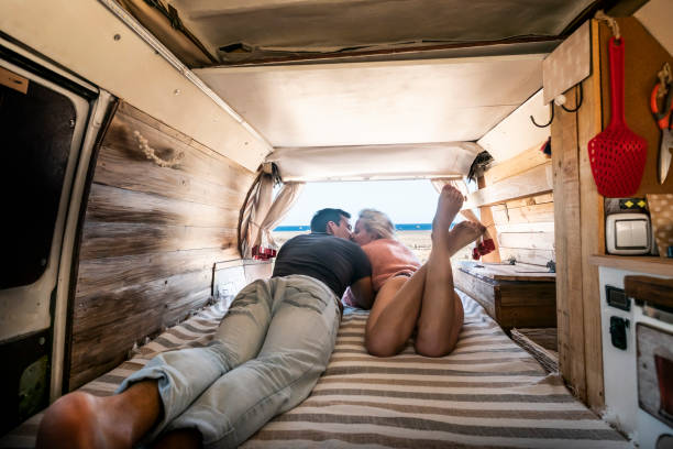 couple lay down on the bed inside a vintage van - summer alternative holiday vacation with young people in love parked in front of a sunny beach and blue free horizon sky - cargo canarias imagens e fotografias de stock