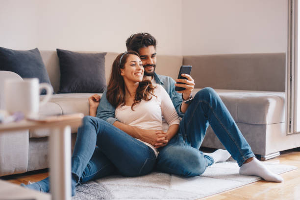 couples regardant le téléphone portable à la maison. - couple photos et images de collection