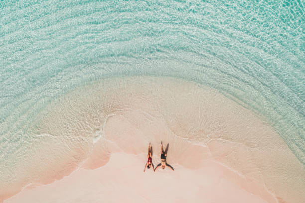 Couple lying on famous pink beach in Komodo national park. Turquoise mint color clear water, tropical vacations on honeymoon. Drone aerial view from above. stock photo